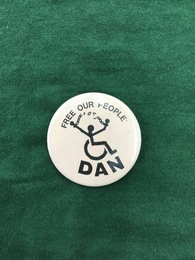 Photo of a badge with the slogan Free Our People, from the Disabled Peoples Direct Action Network