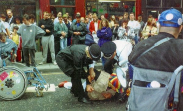 Photo: protester on the ground being arrested at DAN's disabled people's parking protest, Dale Street Liverpool, 1994