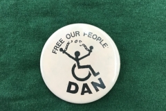 Photo of a badge with the slogan Free Our People, from the Disabled Peoples Direct Action Network