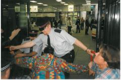 Colour photo of two police officers hold back disabled protestors at two large glass doors, with people inside the building looking on.